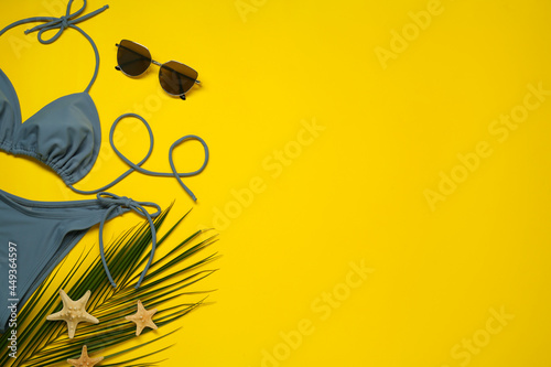 Stylish blue bikini, sunglasses and starfishes on yellow background, flat lay. Space for text