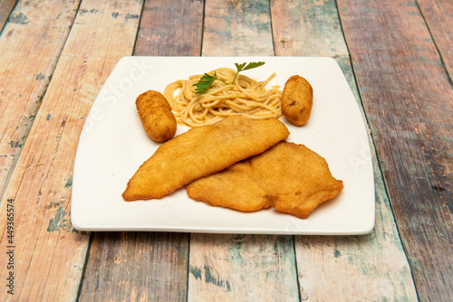 Combination dish with breaded chicken entrecote, croquettes stuffed with béchamel and Iberian ham and spaghetti with cheese on a square white plate