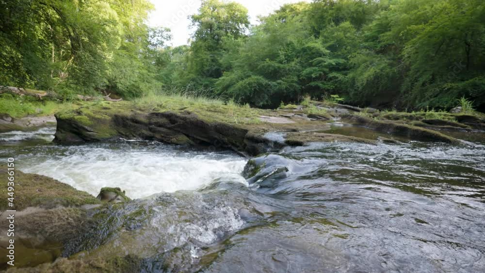 Beginning of river rapids curving around an interesting rock formation. Fast water flow in a river down a small waterfall. Forest setting, slow motion shot. Beginning of river rapids curving around an interesting rock formation. Fast water flow in a river down a small waterfall. Forest setting, slow motion shot.