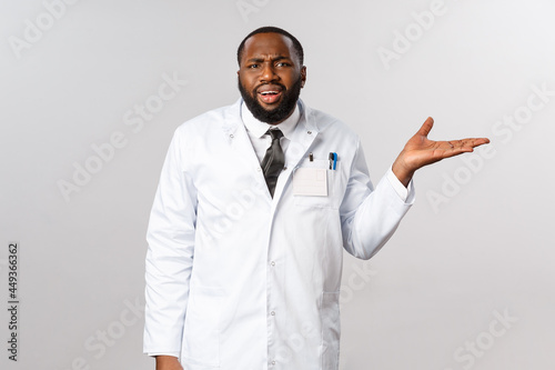 Coronavirus, covid19 and healthcare concept. So what. African-american annoyed doctor arguing or being frustated about people not follow pandemic restrictions, raise hand in dismay, grimacing photo