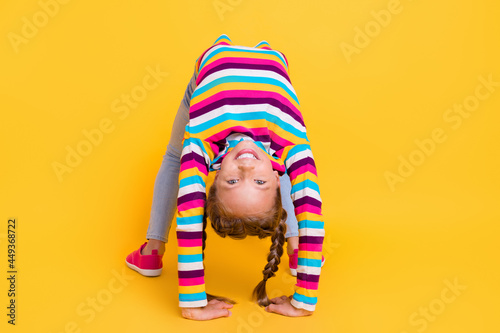 Photo of adorable girl stay bridge toothy smile wear striped shirt jeans footwear isolated yellow color background