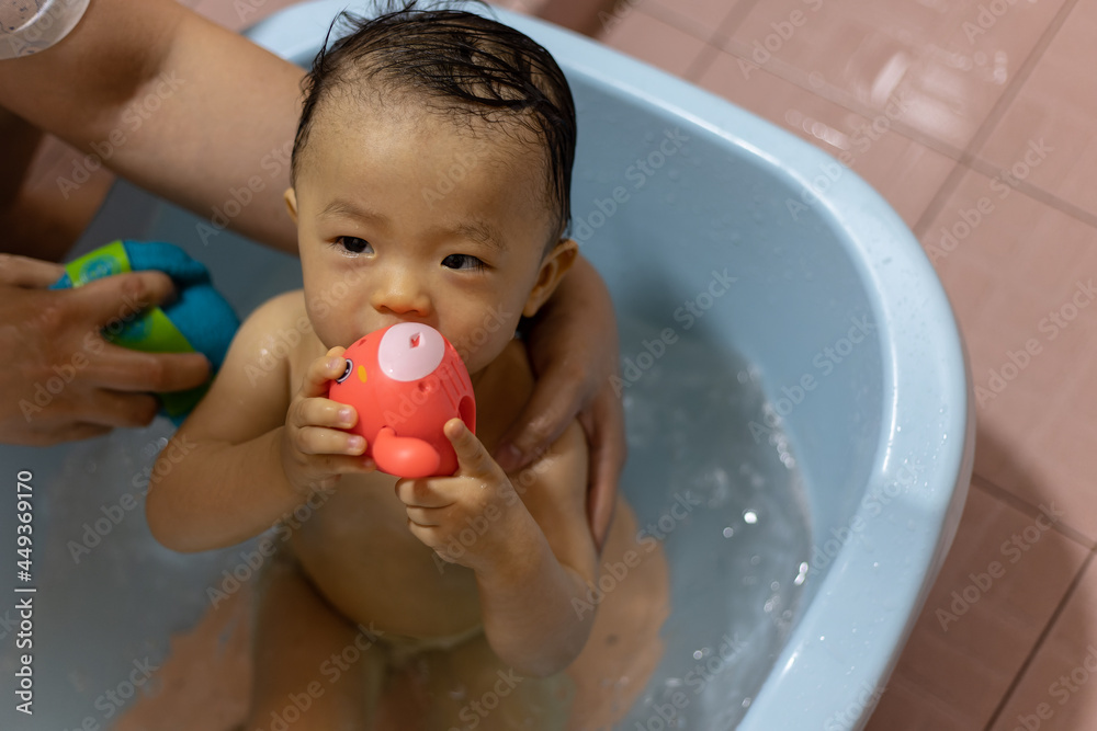 adorable baby boy taking bath in blue tub with toy on hand adorable baby boy taking bath in blue tub with toy on hand