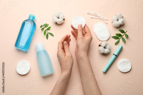 Woman holding cotton pad near makeup removal products on beige background, top view