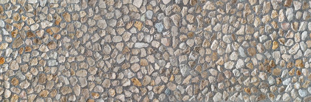 Element einer industriell gefertigten Steinwand aus vielen mittelgroßen Natursteinen in grauem Beton 
