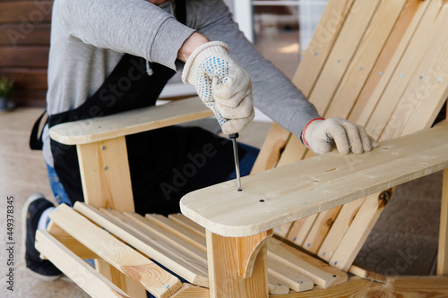 Obraz na plátně Professional carpenter assembling wooden adirondack chair with screwdriver