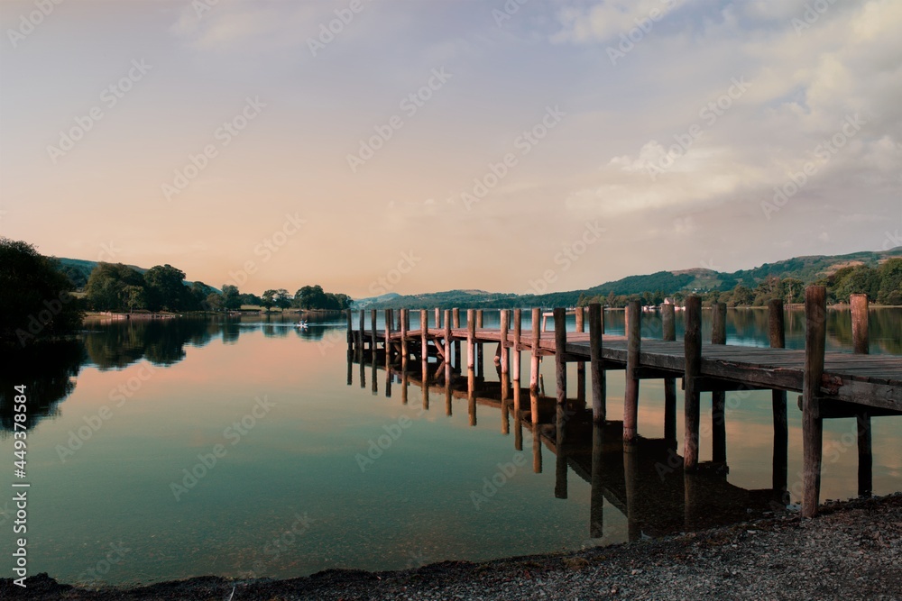 Sunrise over Coniston Water with beautiful pink colours washing over a wooden pier, reflected on the surface of the lake