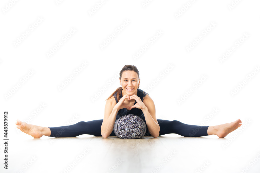 Restorative yoga with a bolster. Young sporty female yoga instructor in bright white yoga studio, lying on bolster cushion, stretching, smilling, showing love and passion for restorative yoga