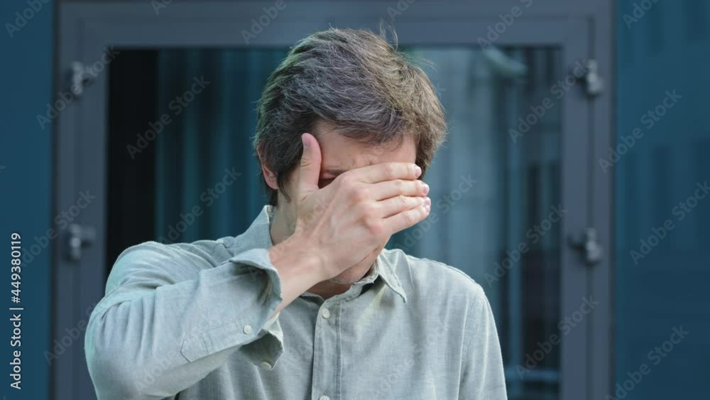 Young man businessman employer covering hiding face, eyes with hands peeping through fingers because of bright sun, does not want to see what is in front of him, refuses to look. Guy shocked concept Young man businessman employer covering hiding face, eyes with hands peeping through fingers because of bright sun, does not want to see what is in front of him, refuses to look. Guy shocked concept