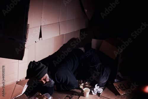 A homeless bearded man sits on boxes on the street and asks for help. Need a homeless person asks for money for food and overnight. © alexkich