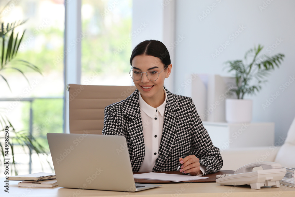 Secretary working with laptop at wooden table in office Secretary working with laptop at wooden table in office