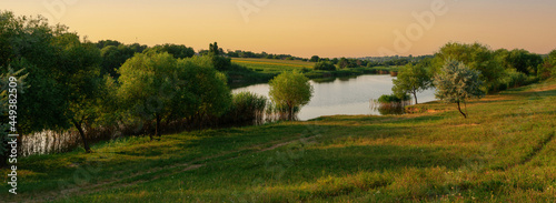 Rural landscape, panorama, banner - small country lake with a meadow and green forest in the background