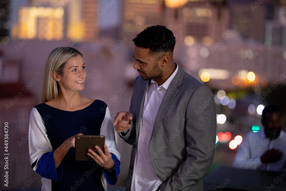 Diverse male and female business colleagues working at night using tablet and talking