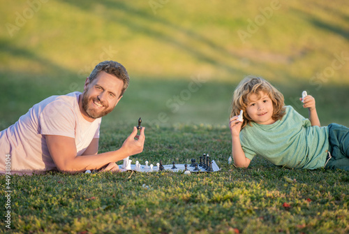 happy family of father man and son kid playing chess on green grass in park outdoor, friendship