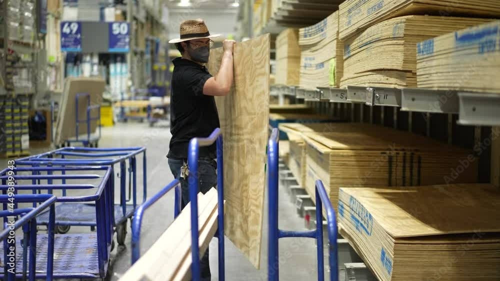 Home improvement man chooses sheet of plywood and puts it on his shopping cart in big box hardware store.