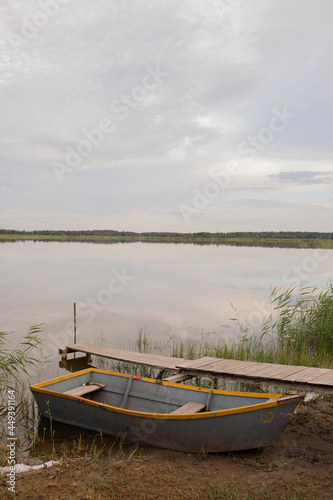 A wooden boat stands at a make-up pier on the shore of a lake near the edge of the village.
