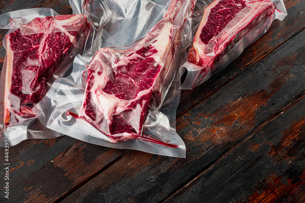 Raw beef dry aged steak vacuum sealed bag for sell, tomahawk, t bone and club steak cuts, on old dark  wooden table background, with copy space for text