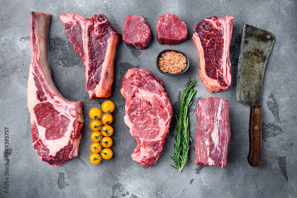 Raw beef meat steaks, tomahawk, t bone, club steak, rib eye and tenderloin cuts, on gray stone background, top view flat lay