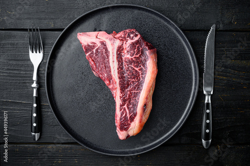 Dry aged t bone marbled beef steak, on plate, on black wooden table background, top view flat lay
