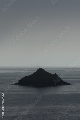 Lone Island stands against a moody background of the sea in the rain on the north Cornwall coast - silhouetted