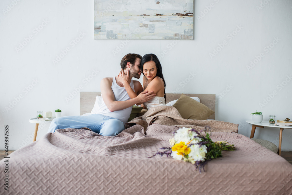 bouquet of flowers on bed near pleased couple hugging on bed