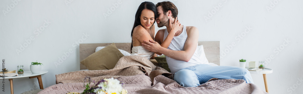 pleased couple hugging near bouquet of flowers on bed, banner pleased couple hugging near bouquet of flowers on bed, banner