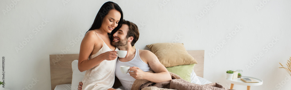 happy couple holding cups of coffee in bed, banner happy couple holding cups of coffee in bed, banner