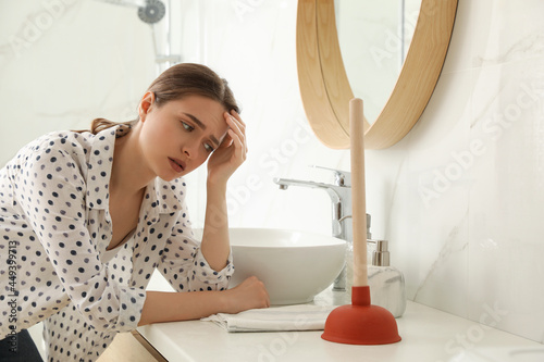 Papier peint Unhappy young woman with plunger near clogged sink in bathroom