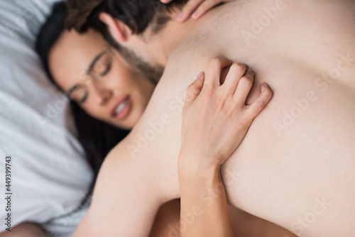 blurred and passionate woman making out with shirtless man in bedroom