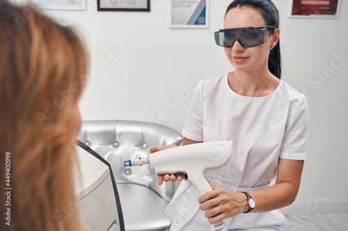 Smiling cosmetologist using laser device for woman
