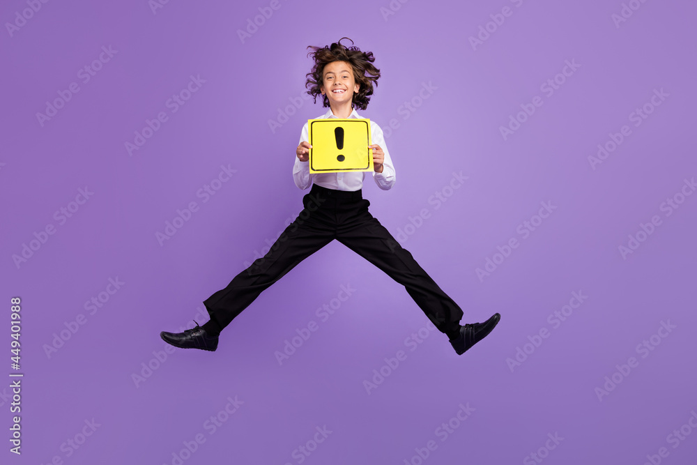 Full size photo of funny little brunet boy jump hold sign wear shirt trousers sneakers isolated on purple color background