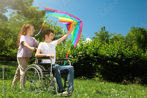 Happy teenage boy in wheelchair with kite and girl at park on sunny day