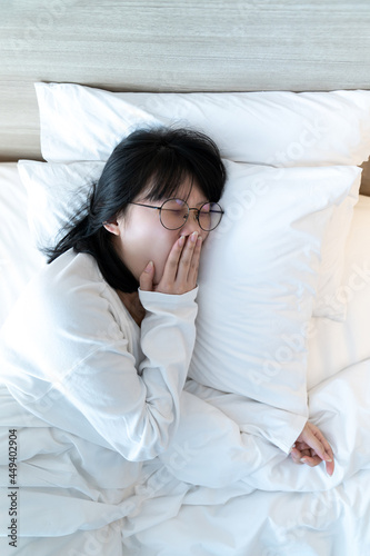 Glasses Asian woman are yawning after waked up on the bed in the morning time.