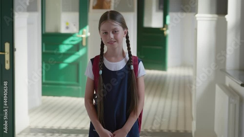 Portrait of smiling caucasian schoolgirl standing in school corridor wearing schoolbag.