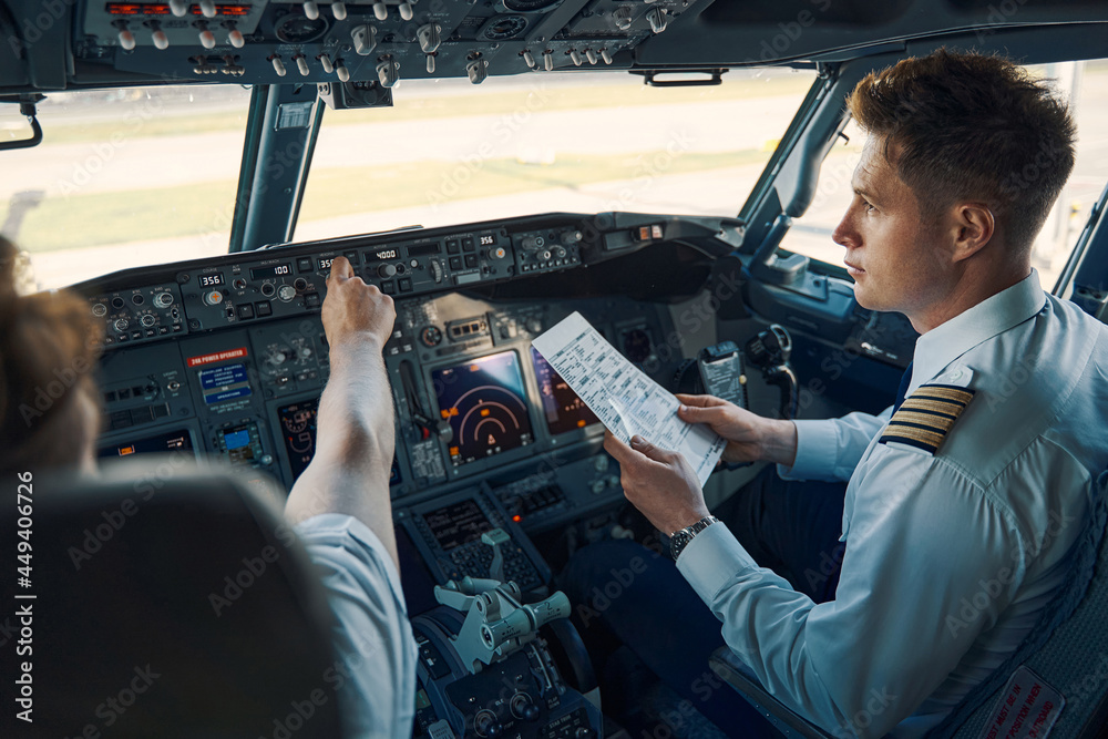 Airline captain and first officer sitting in the cockpit - obrazy, fototapety, plakaty 