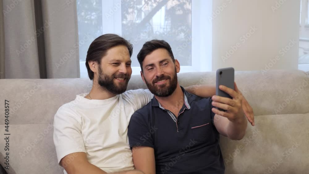 Young cute caucasian men homosexual couple using smartphone making video call or selfie on the couch with happiness at home, lgbt, homosexual gay couple diversity lifestyle copy space.