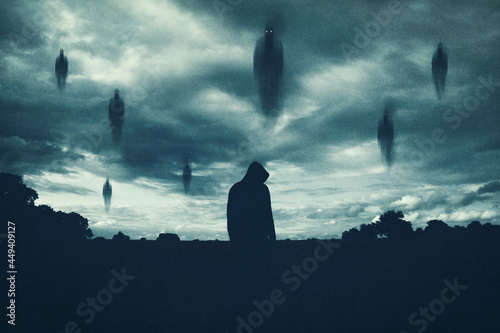 A supernatural concept. Of spirits floating above a hooded figure in the countryside at night. With a grunge, textured edit. photo