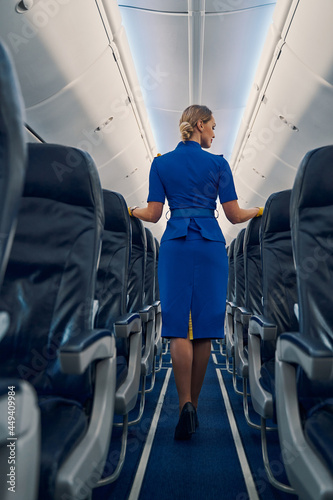 Blonde air hostess in uniform standing in the cabin aisle photo