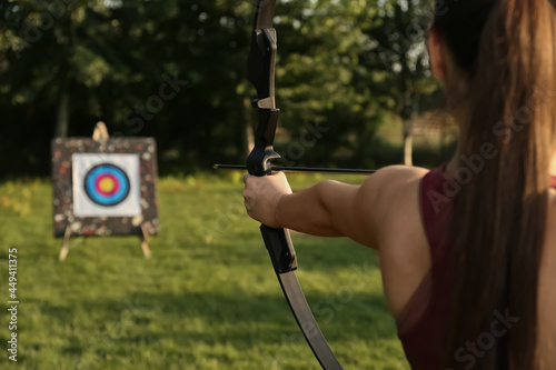 Woman with bow and arrow aiming at archery target in park, closeup photo