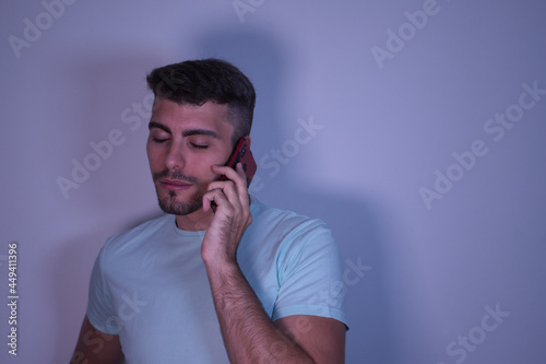 Young Hispanic man talking on his mobile phone with his eyes closed because of bad news on white background.