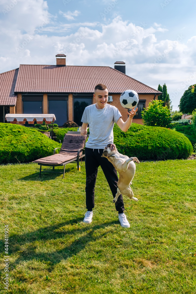 Young caucasian man with amputated arm and prosthesis playing with his dog with a soccer ball in the backyard of his house, vertical orientation