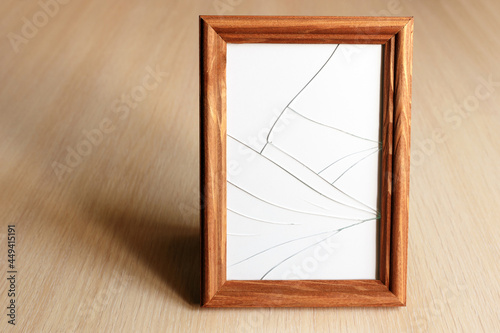 Cracked glass. Wooden frame for the picture. Light wood surface.