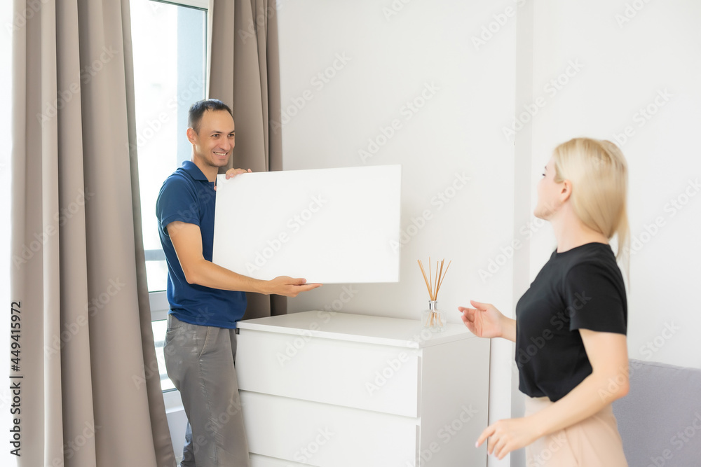 Excited young husband and wife hang frame picture on wall happy settling together moving to new house, overjoyed biracial couple decorating own home relocating, ownership concept Excited young husband and wife hang frame picture on wall happy settling together moving to new house, overjoyed biracial couple decorating own home relocating, ownership concept