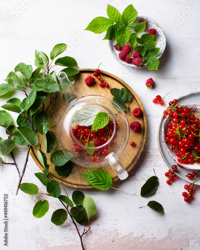 A warm drink on a light background. Berry tea with raspberries and red currants. Tea made from berries in a teapot. Summer still life with leaves and tea. Fresh raspberry harvest