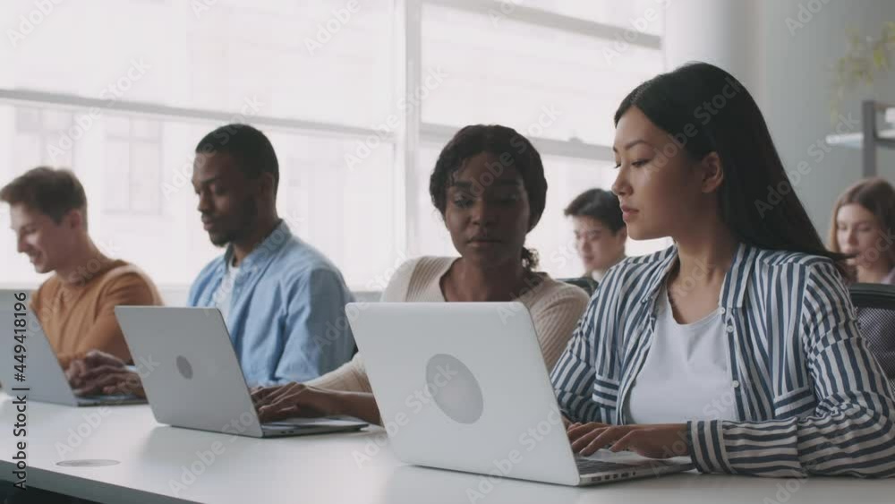 Young asian girl having troubles during lesson, asking her black groupmate for help, typing on laptops at college Young asian girl having troubles during lesson, asking her black groupmate for help, typing on laptops at college