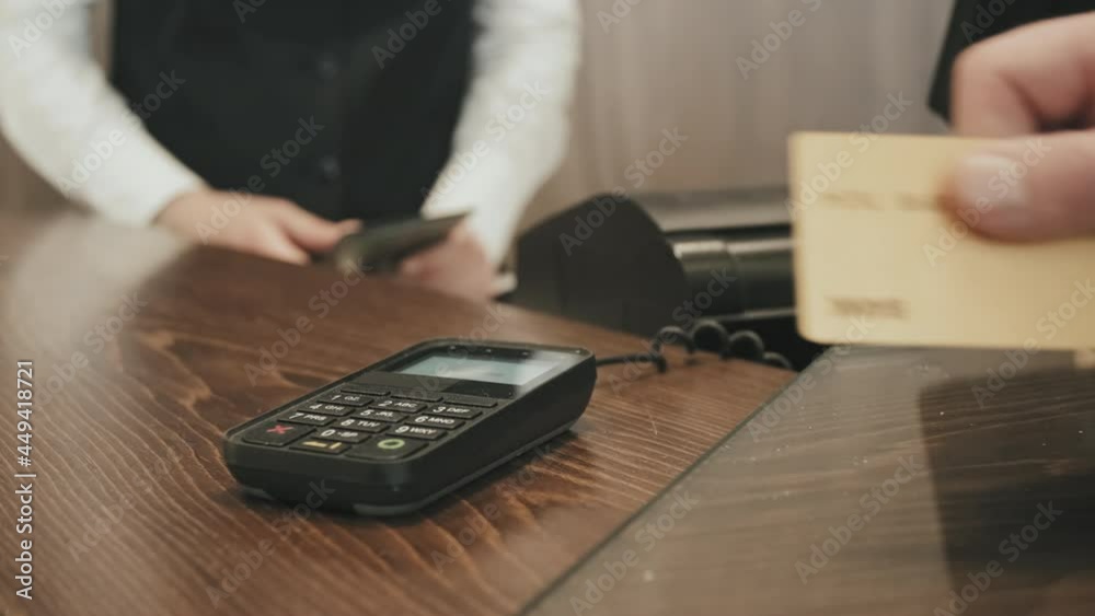 Slowmo close-up of unrecognizable man attaching credit card to terminal for making contactless payment at hotel reception desk