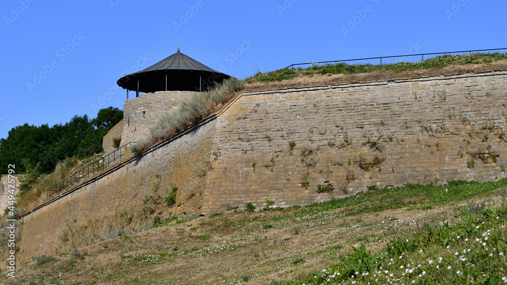 Medieval South-west corner tower XV-XVI c. Narva Castle, Estonia, and an earthen rampart with a limestone wall on a sunny early summer morning under a blue sky. Medieval South-west corner tower XV-XVI c. Narva Castle, Estonia, and an earthen rampart with a limestone wall on a sunny early summer morning under a blue sky.