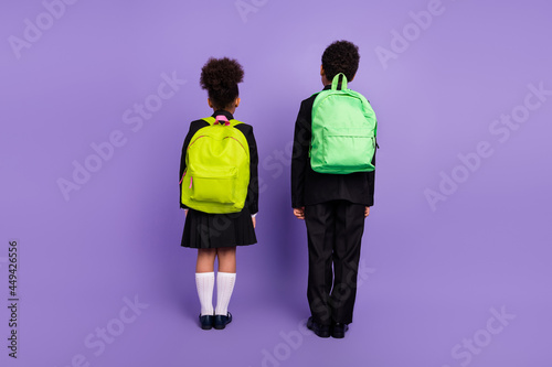 Rear back view photo of two african people kids go school wear backpack uniform isolated violet color background © deagreez