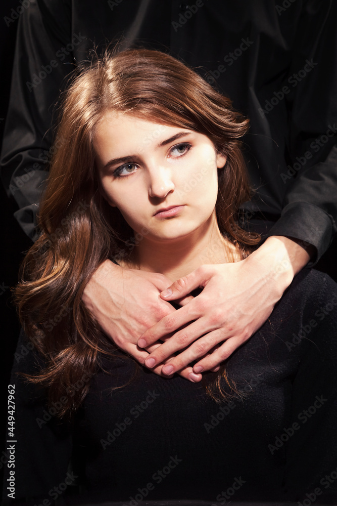 Naklejka premium Portrait of a young girl, male hands lie on her shoulders, black background