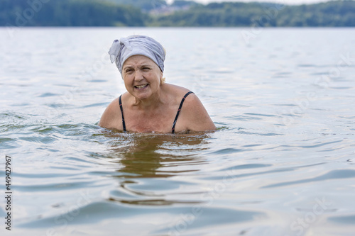 An elderly lady swims in a calm lake. Aged woman enjoying swimming in warm lake water at the resort © Ilya