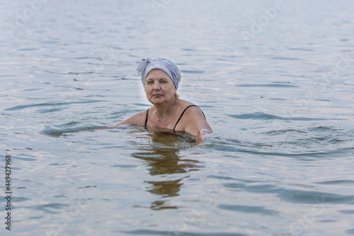 An elderly lady swims in a calm sea. Aged woman enjoying swimming in warm sea water at the resort © Ilya